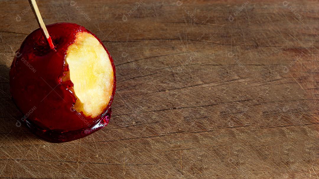 Maçã do amor caramelada, mordida sobre mesa