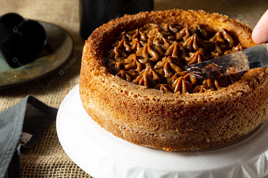 mão de homem cortando uma fatia de bolo de churros brasileiro típico com doce de leite, em uma mesa, café da manhã confortável ou cena de lanche