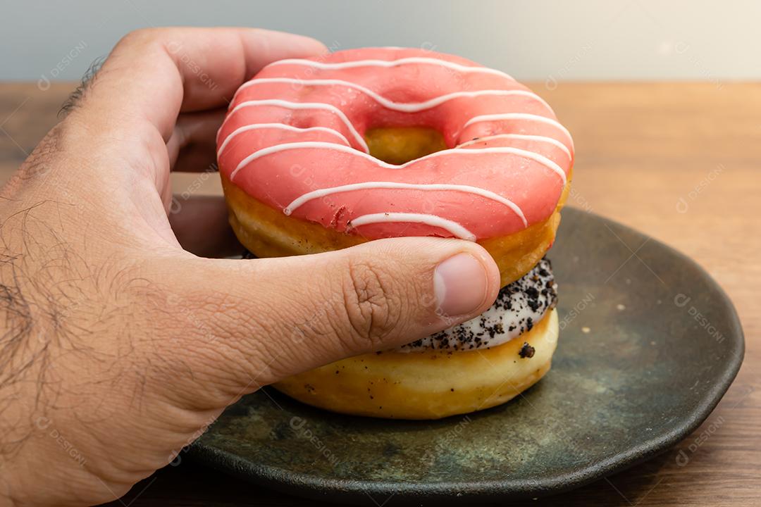 Mão masculina segurando bolinhos donuts everglazed sobre mesa madeira fundo branco