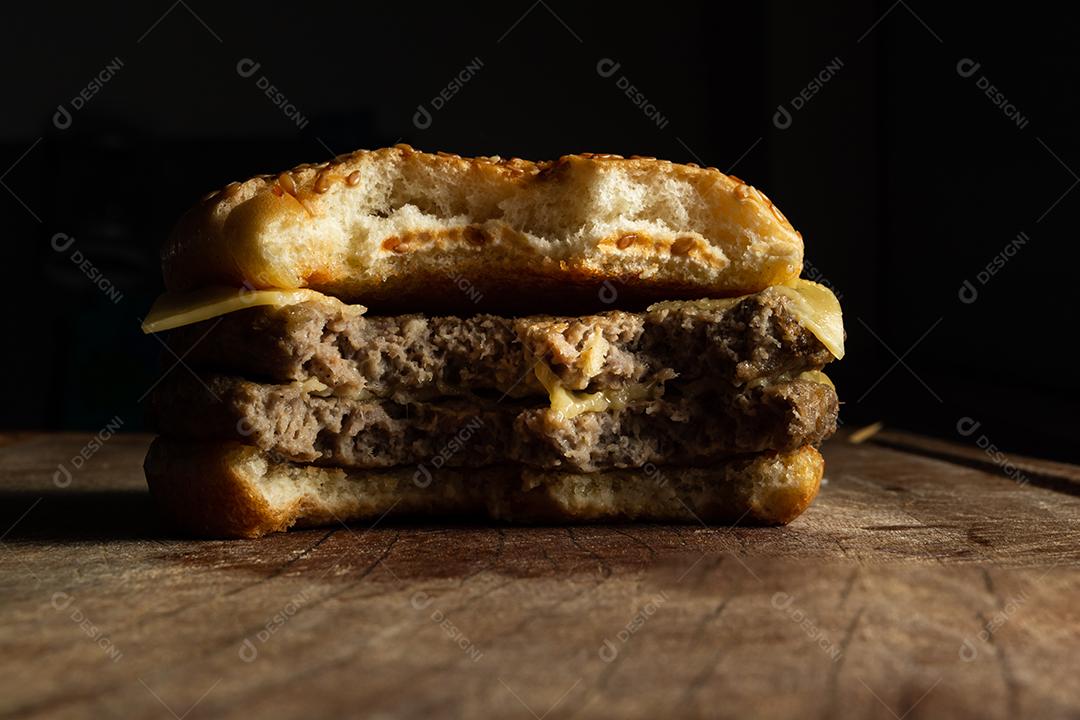Hambúrguer de carne grelhada, queijo mordido sobre mesa madeira fundo preto