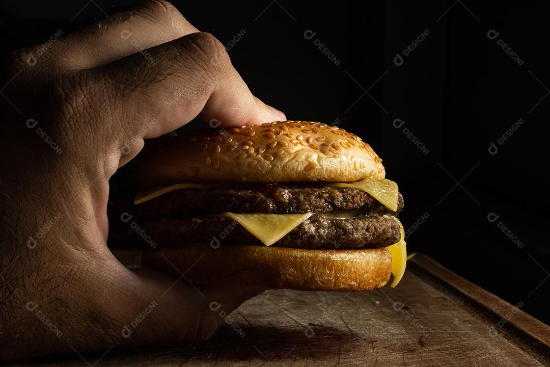 Hamburguer carne grelhada, queijo mão masculino segurando sobre mesa madeira fundo preto