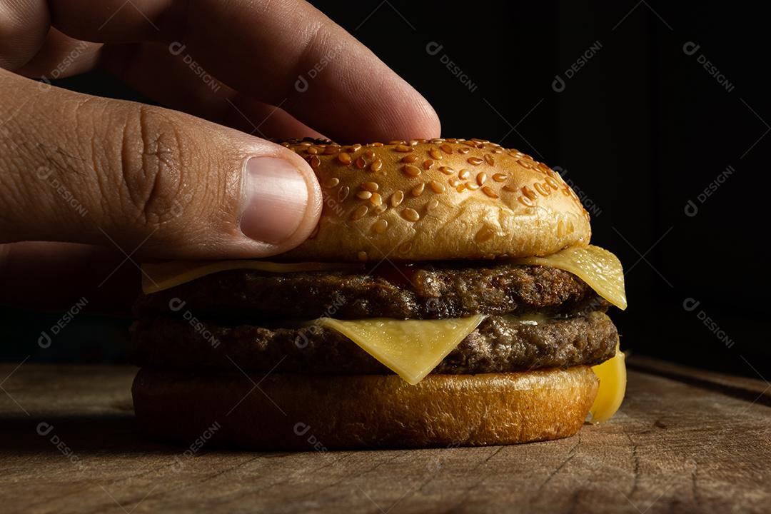 Hambúrguer ,carne grelhada, queijo com mão masculino segurando  sobre mesa madeira fundo preto