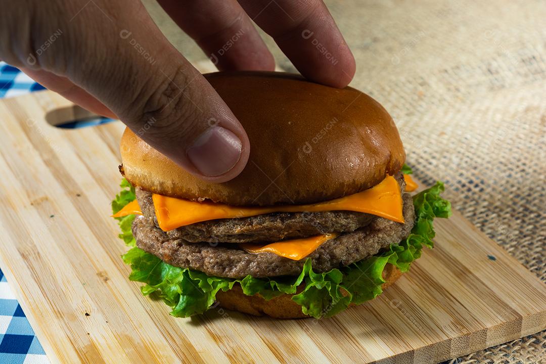 mão masculina terminando um cheeseburger com pão superior.