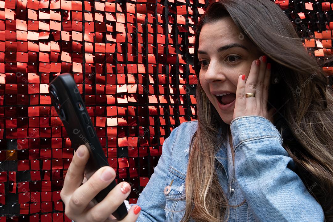 Mulher usando telefone celular e impressionada em fundo azul brilhante