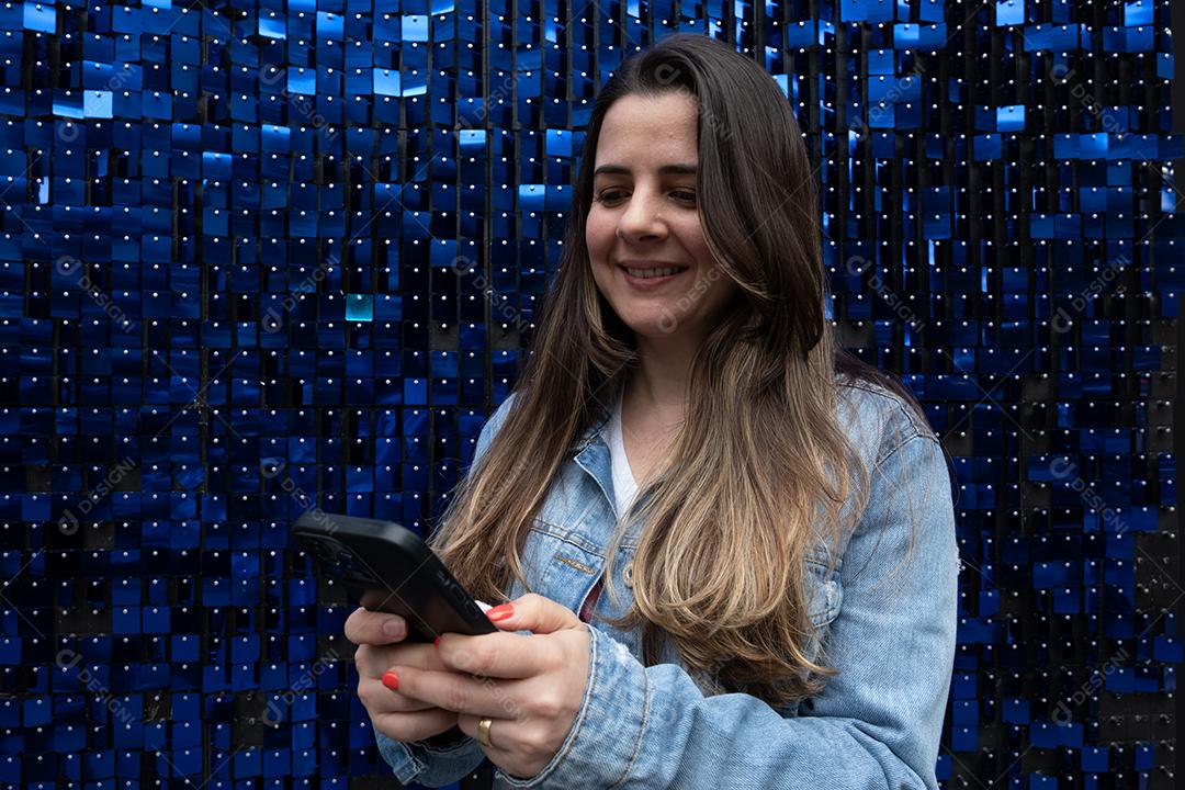 Mulher usando telefone celular e sorrindo em fundo azul brilhante