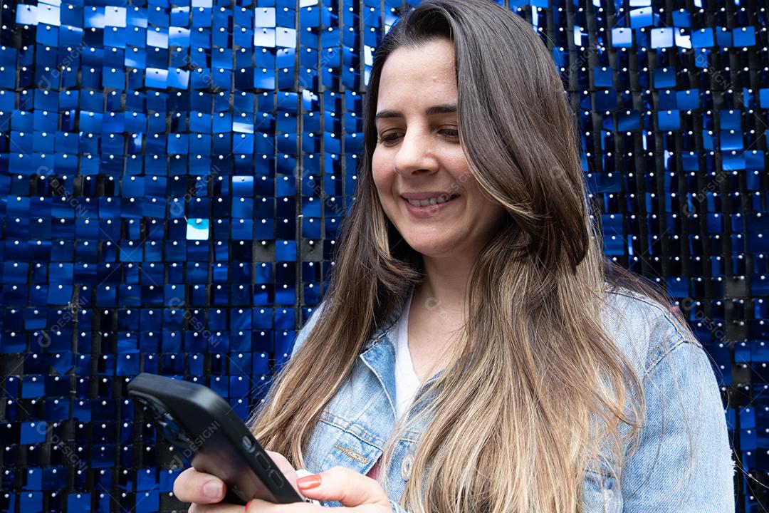 Mulher usando telefone celular e sorrindo em fundo azul brilhante