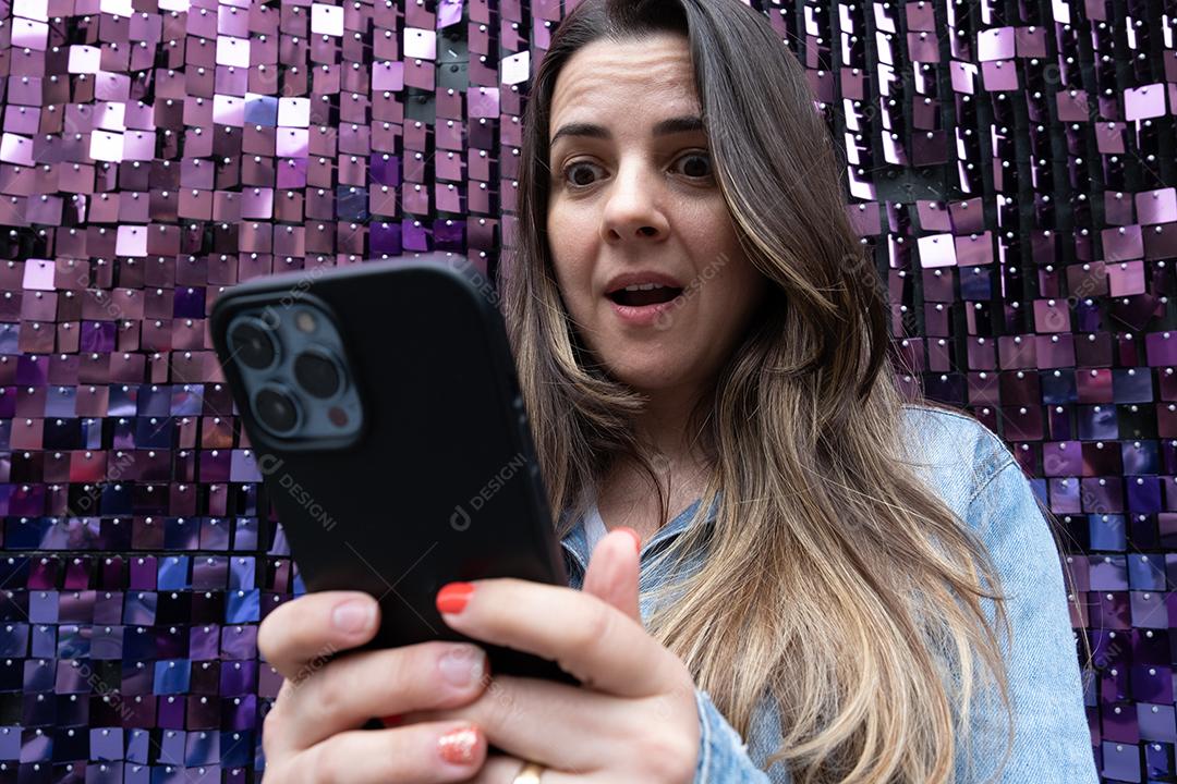 Amazed woman using cell phone and bright purple background