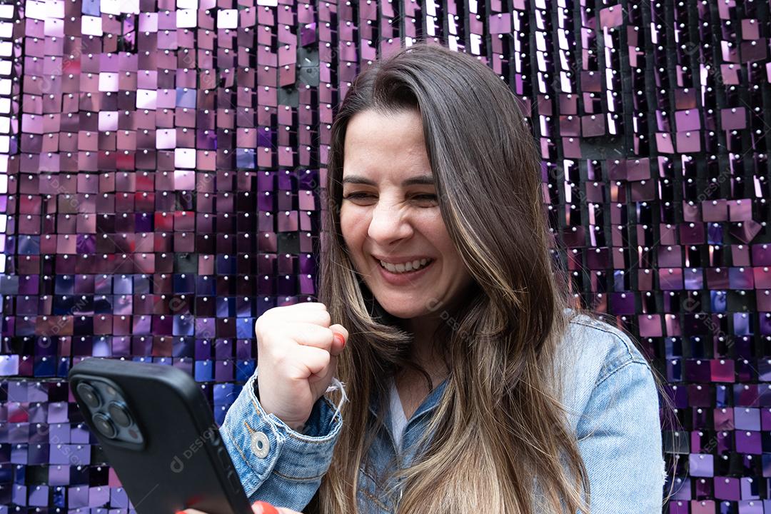 Mulher comemorando usando celular e fundo roxo brilhante