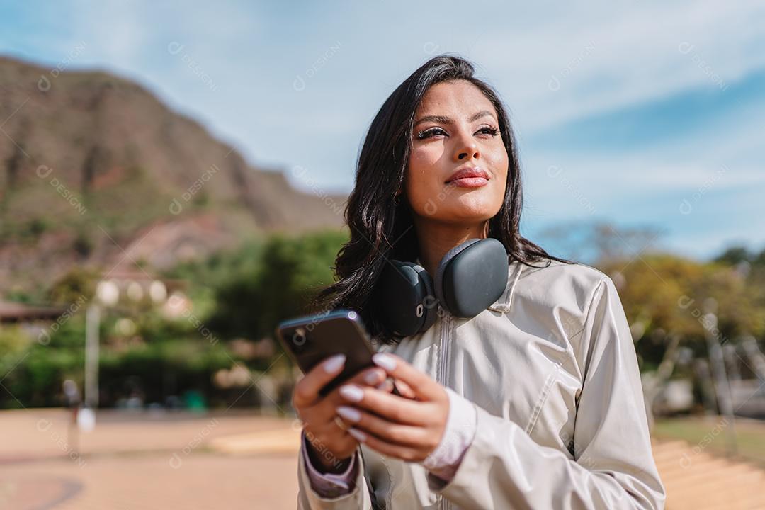 Linda garota latina usando seu celular no parque.