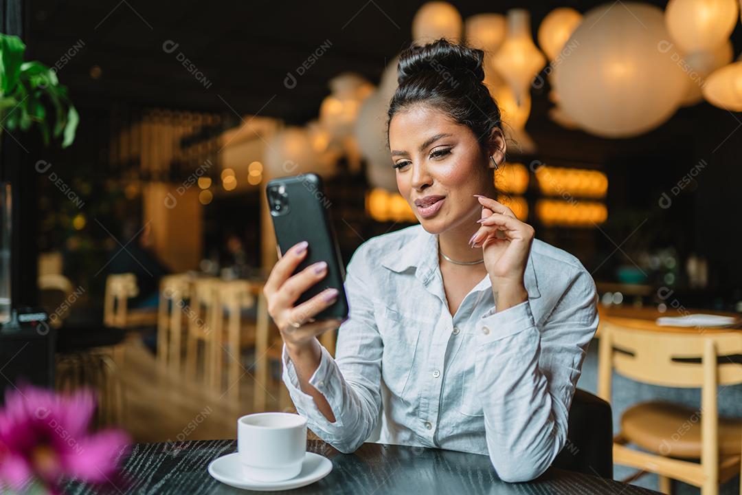 Linda garota latina usando seu celular no café.