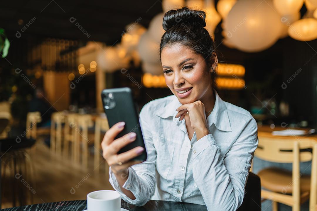 Linda garota latina usando seu celular no café.