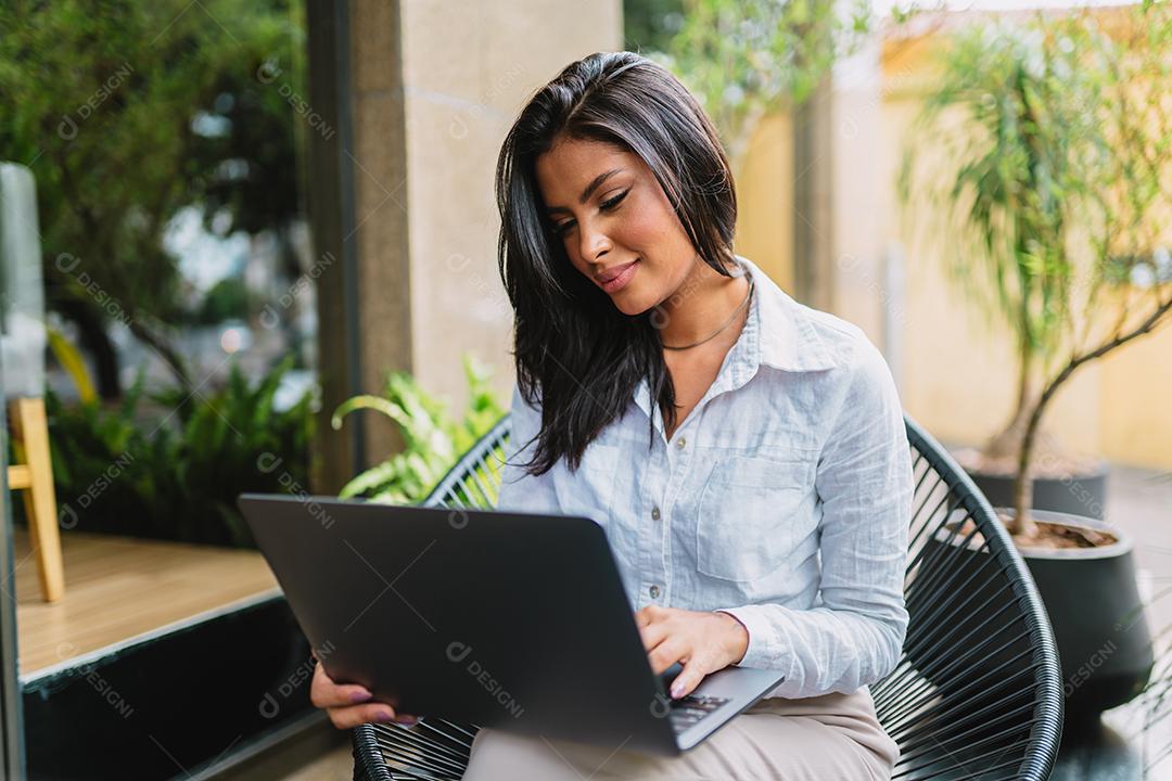 Nomad at work. Confident latin young woman making video call on laptop while sitting by window in cafe.