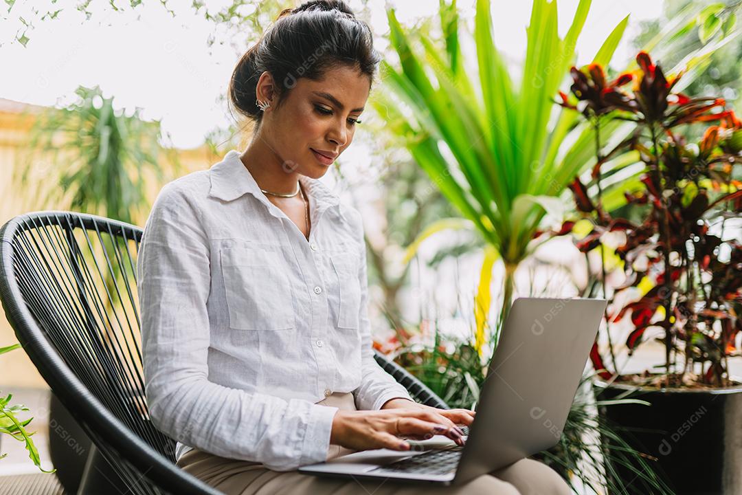 Nômade no trabalho. Confiante jovem latina fazendo videochamada no laptop enquanto está sentado pela janela no café.