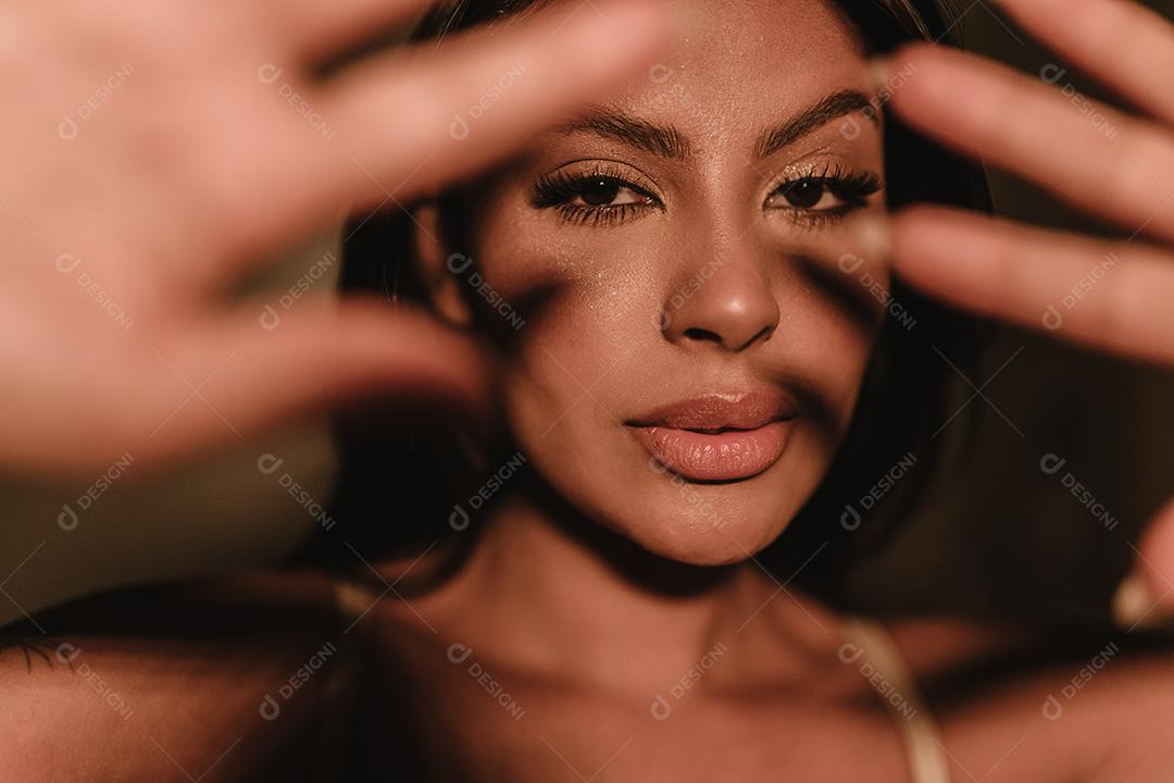 O retrato emocional de uma linda garota latina cobre o rosto com a mão dentro de casa.