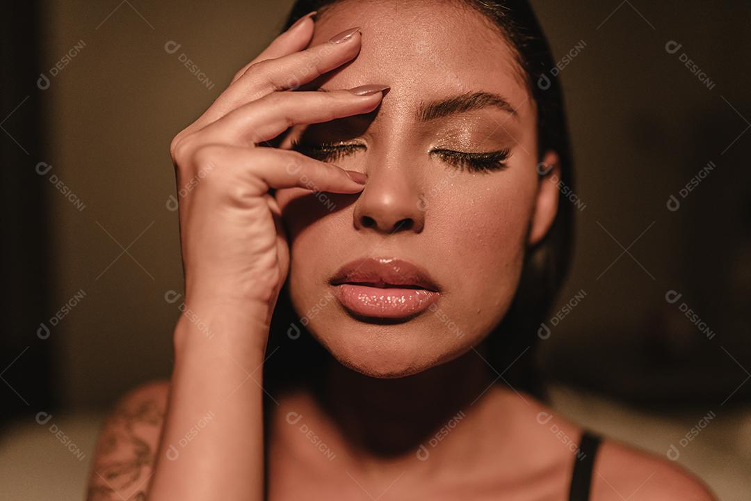 O retrato emocional de uma linda garota latina cobre o rosto com a mão dentro de casa.