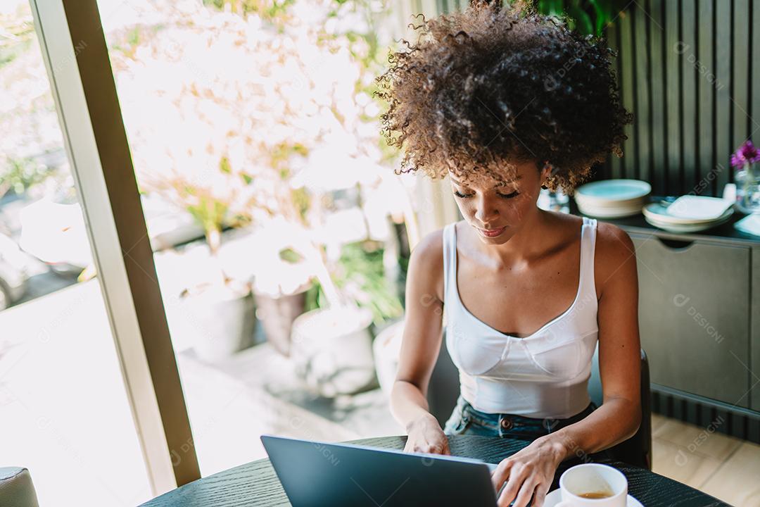 Nômade no trabalho. Confiante jovem latina fazendo videochamada no laptop enquanto está sentado pela janela no café.