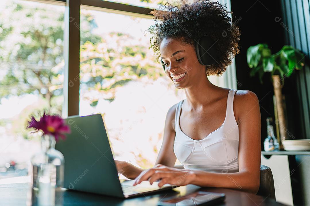 Nômade no trabalho. Confiante jovem latina fazendo videochamada no laptop enquanto está sentado pela janela no café.