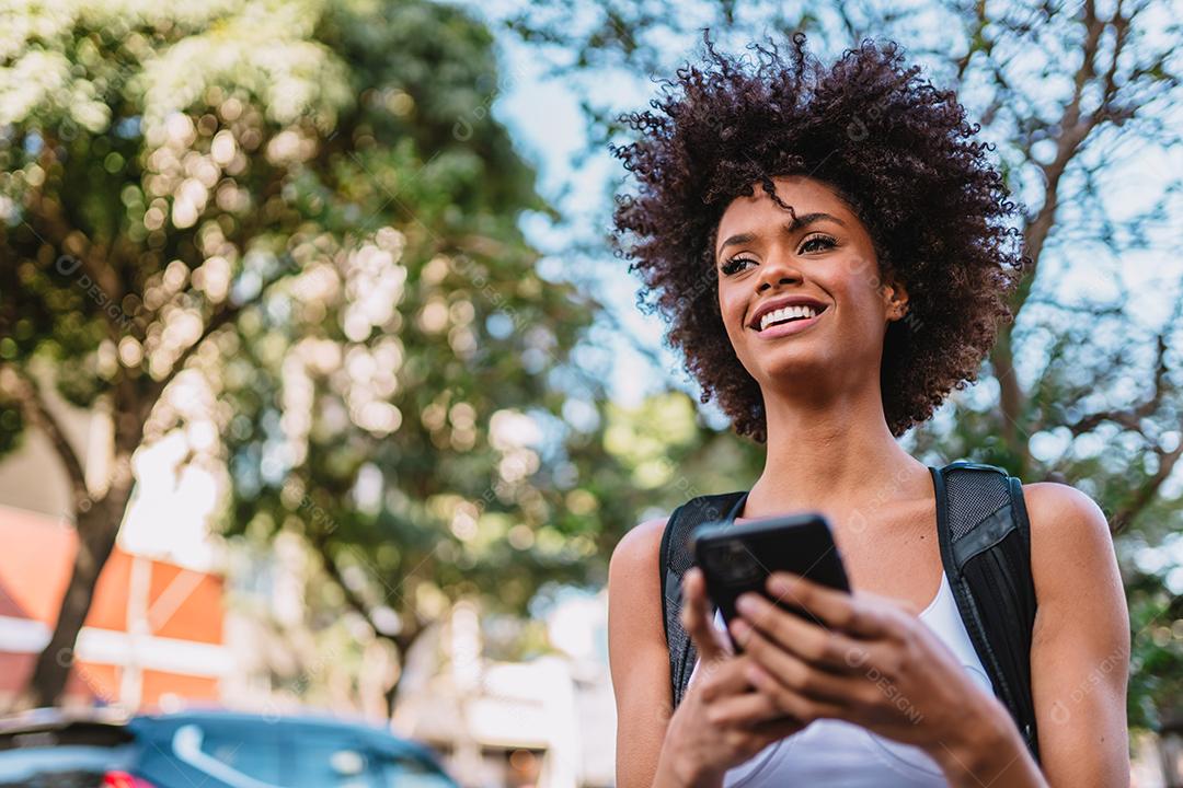 Mulher jovem e bonita Latina usando smartphone em pé na rua da cidade. Retrato de mulher latina sorridente usando telefone celular.