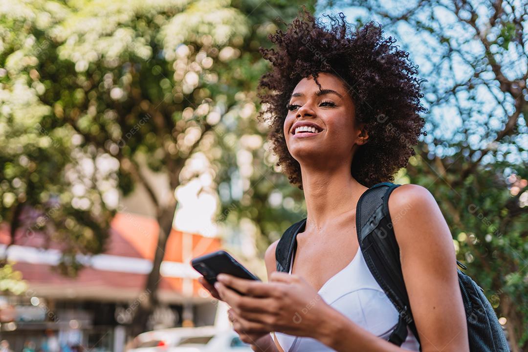 Mulher jovem e bonita Latina usando smartphone em pé na rua da cidade. Retrato de mulher latina sorridente usando telefone celular.