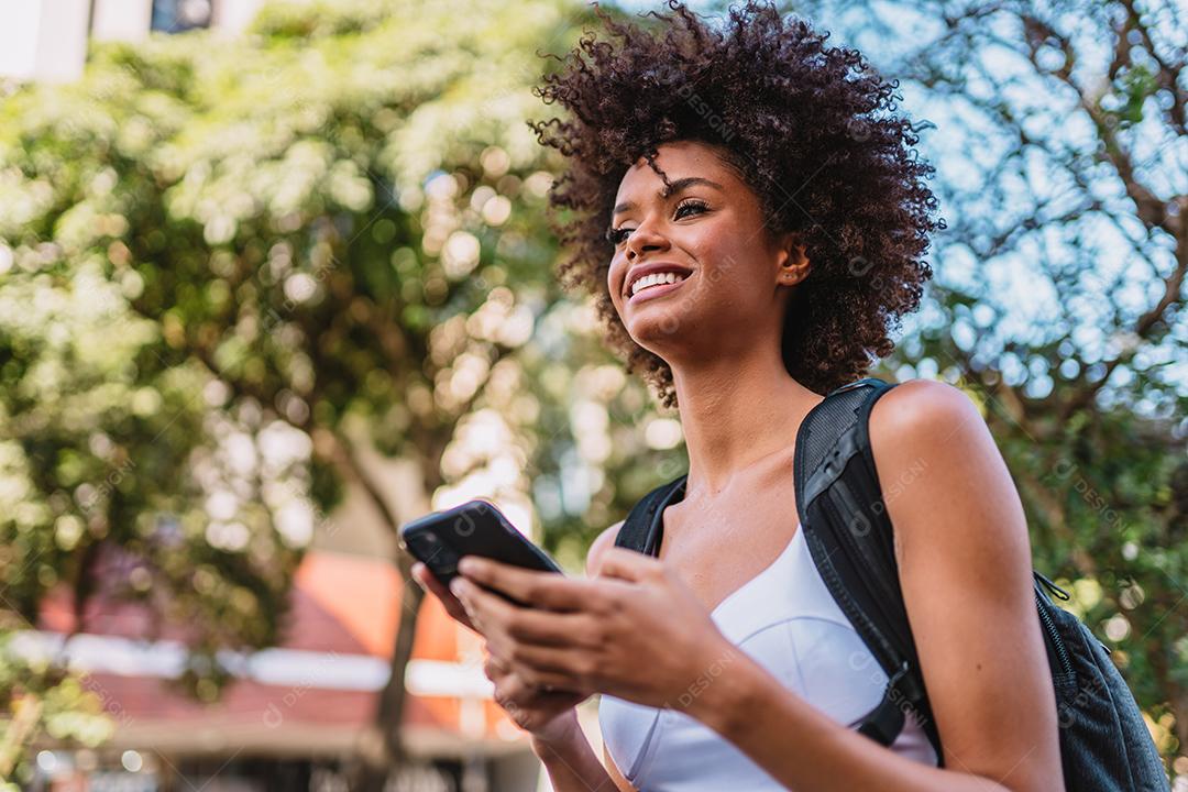 Mulher jovem e bonita Latina usando smartphone em pé na rua da cidade. Retrato de mulher latina sorridente usando telefone celular.
