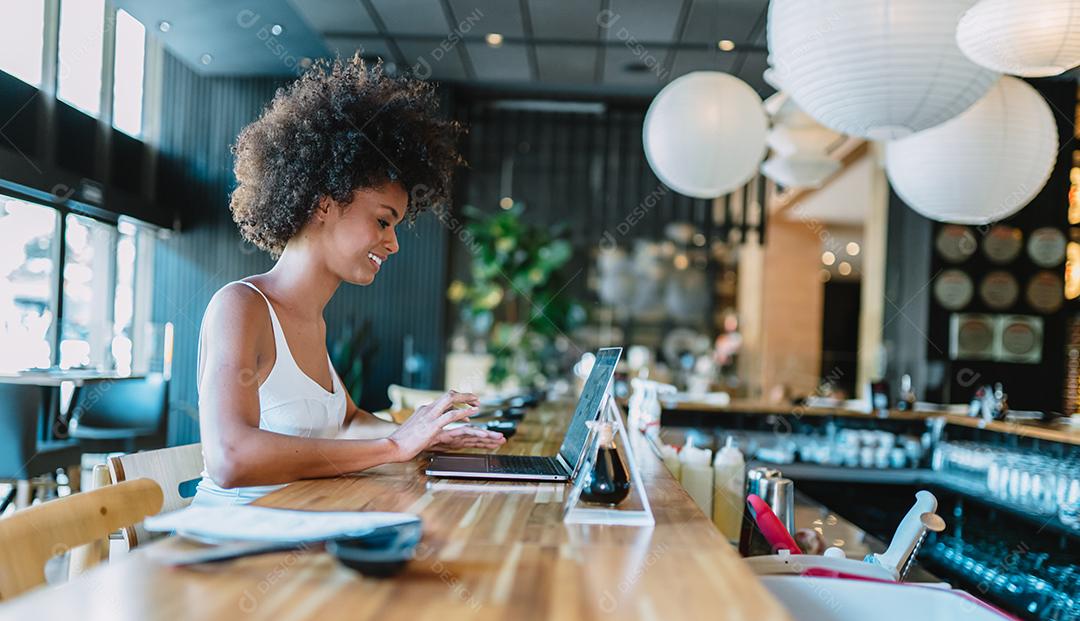 Nômade no trabalho. Confiante jovem latina fazendo videochamada no laptop enquanto está sentado pela janela no café.