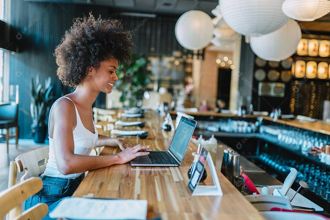Nômade no trabalho. Confiante jovem latina fazendo videochamada no laptop enquanto está sentado pela janela no café.