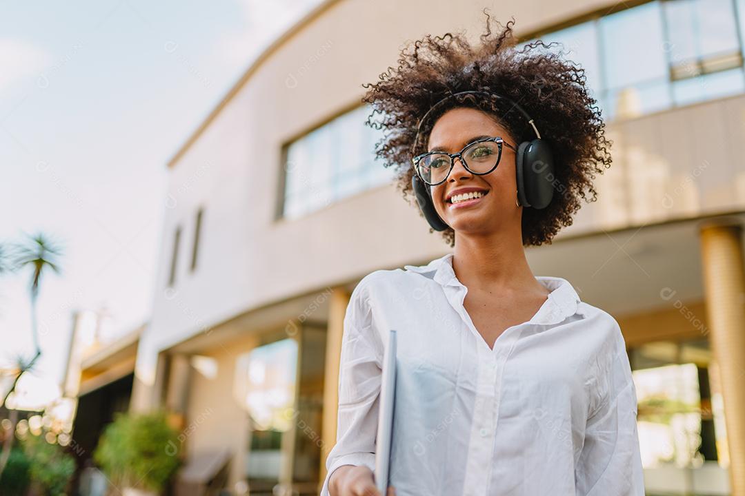 Vista de ângulo baixo da empresária latina sorridente segurando laptop e óculos perto de prédio turva.