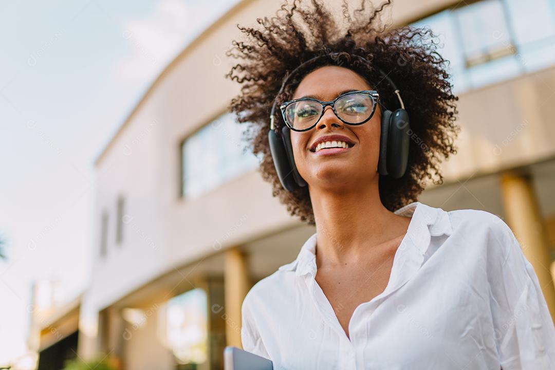 Vista de ângulo baixo da empresária latina sorridente segurando laptop e óculos perto de prédio turva.