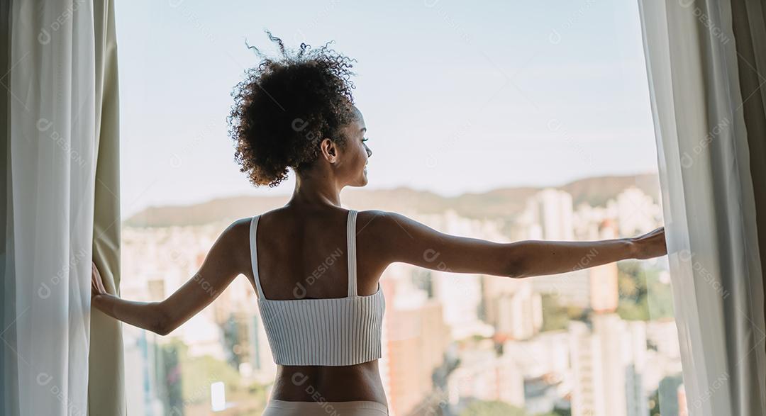 Linda mulher latina acordando de manhã, o sol brilha sobre ela da grande janela.