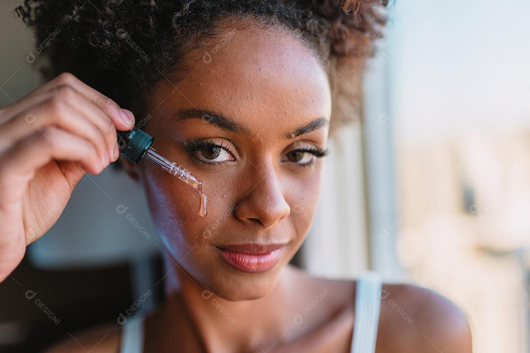 Feche o retrato de uma mulher latina aplicando soro hialurônico no rosto.