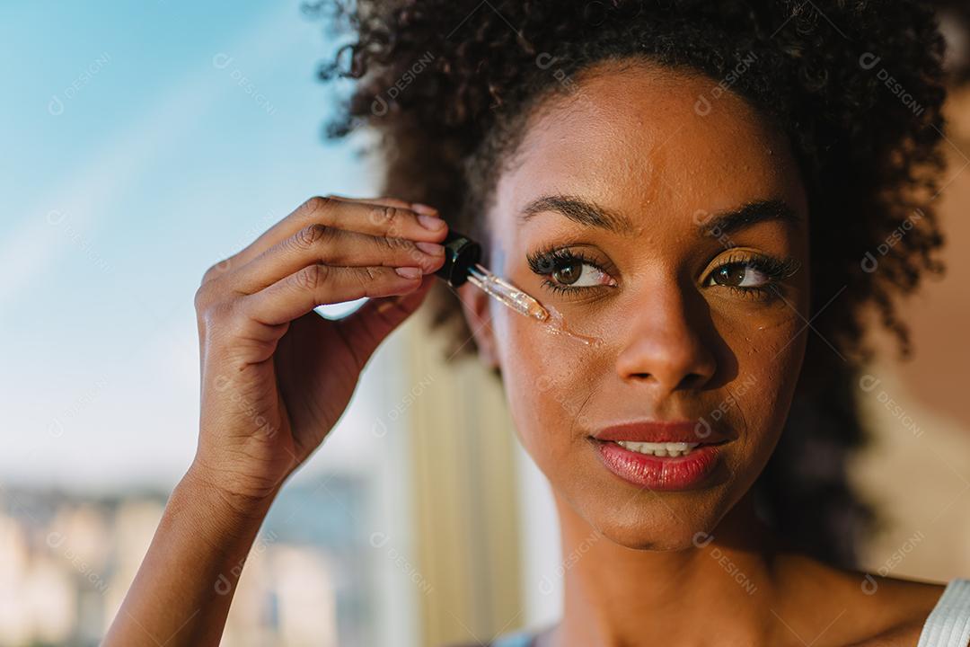 Feche o retrato de uma mulher latina aplicando soro hialurônico no rosto.