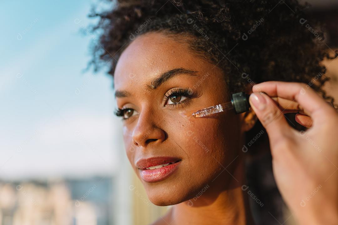 Feche o retrato de uma mulher latina aplicando soro hialurônico no rosto.