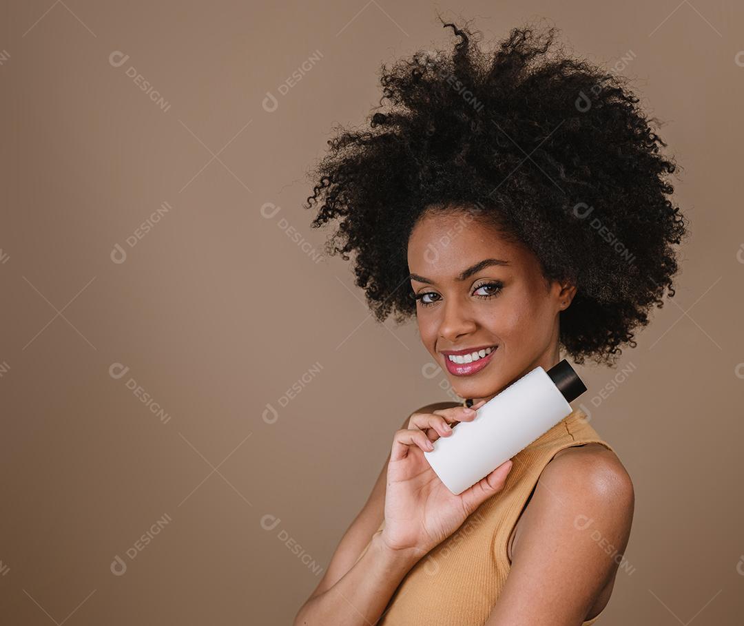 Mulher latina de beleza com penteado afro. mulher brasileira. Segurando a embalagem de xampu em branco