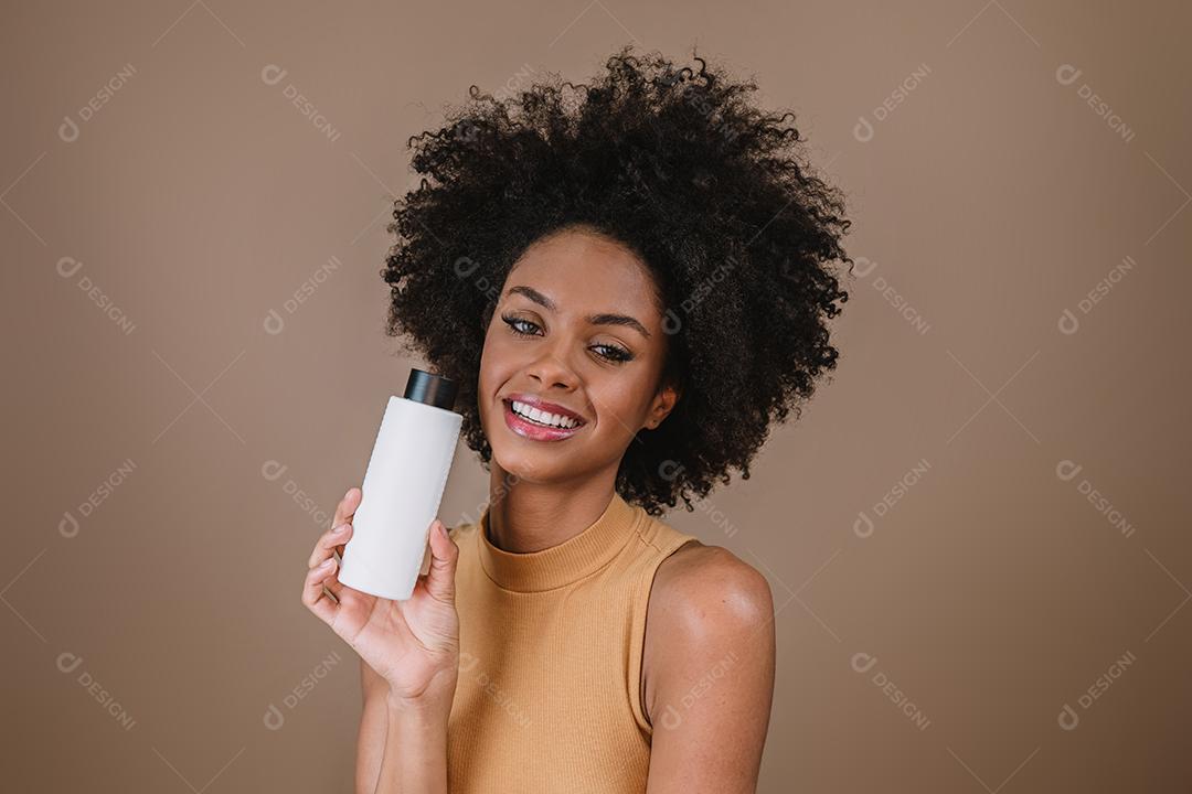 Mulher latina de beleza com penteado afro. mulher brasileira. Segurando a embalagem de xampu em branco
