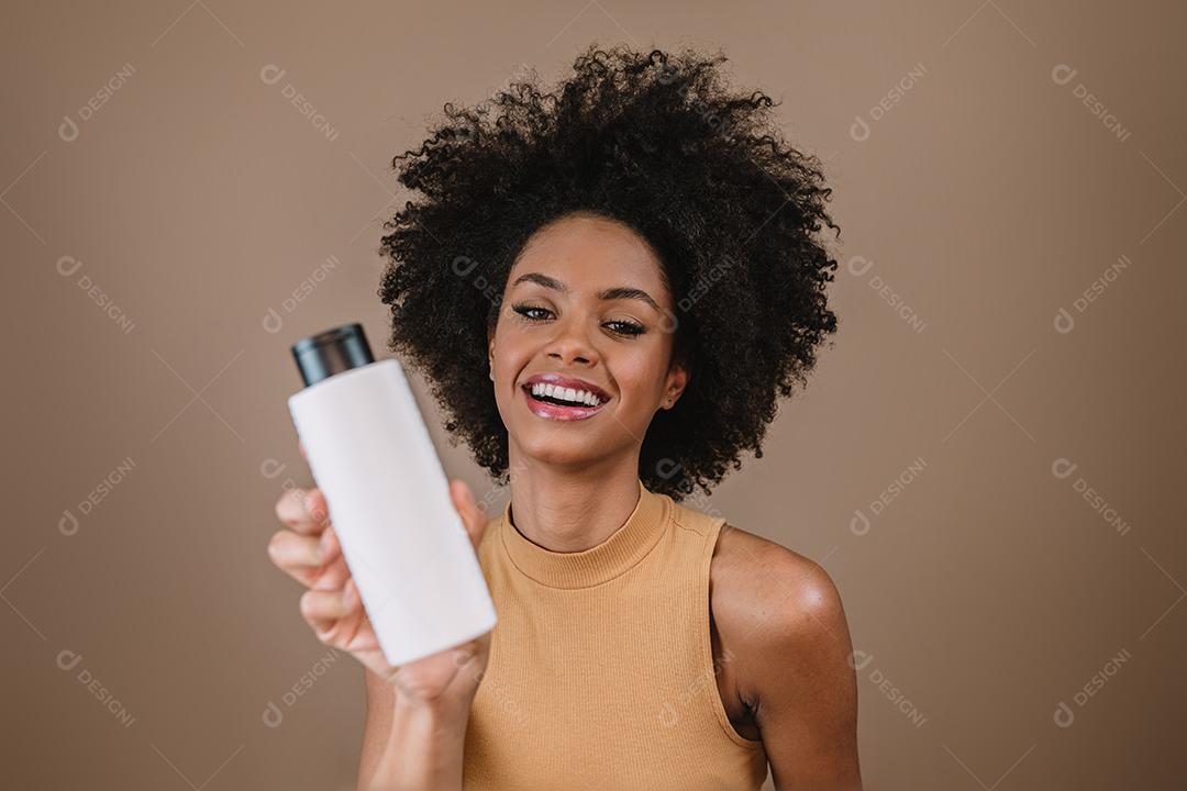 Mulher latina de beleza com penteado afro. mulher brasileira. Segurando a embalagem de xampu em branco