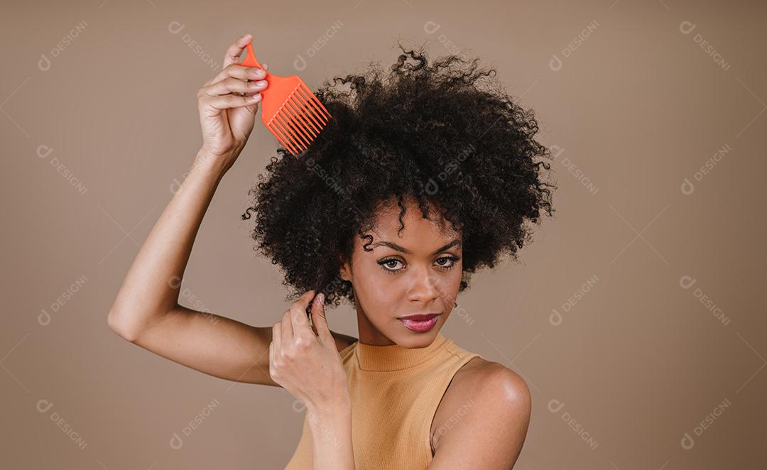Jovem latina penteando o cabelo. Garfo para pentear cabelos cacheados. Fundo pastel.