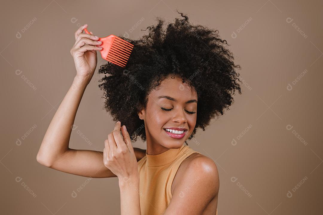 Jovem latina penteando o cabelo. Garfo para pentear cabelos cacheados. Fundo pastel.