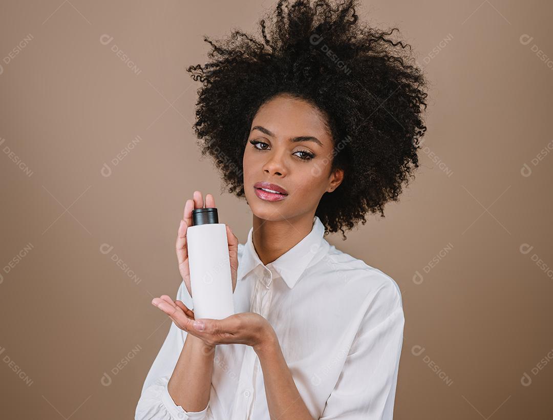 Mulher latina de beleza com penteado afro. mulher brasileira. Segurando a embalagem de xampu em branco