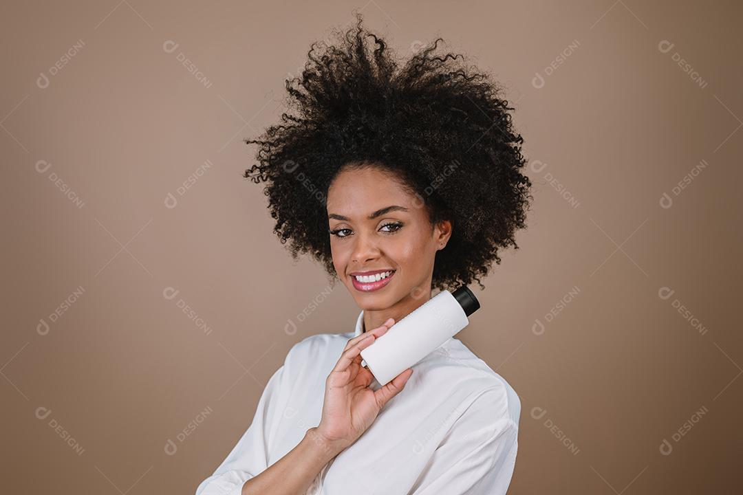 Mulher latina de beleza com penteado afro. mulher brasileira. Segurando a embalagem de xampu em branco
