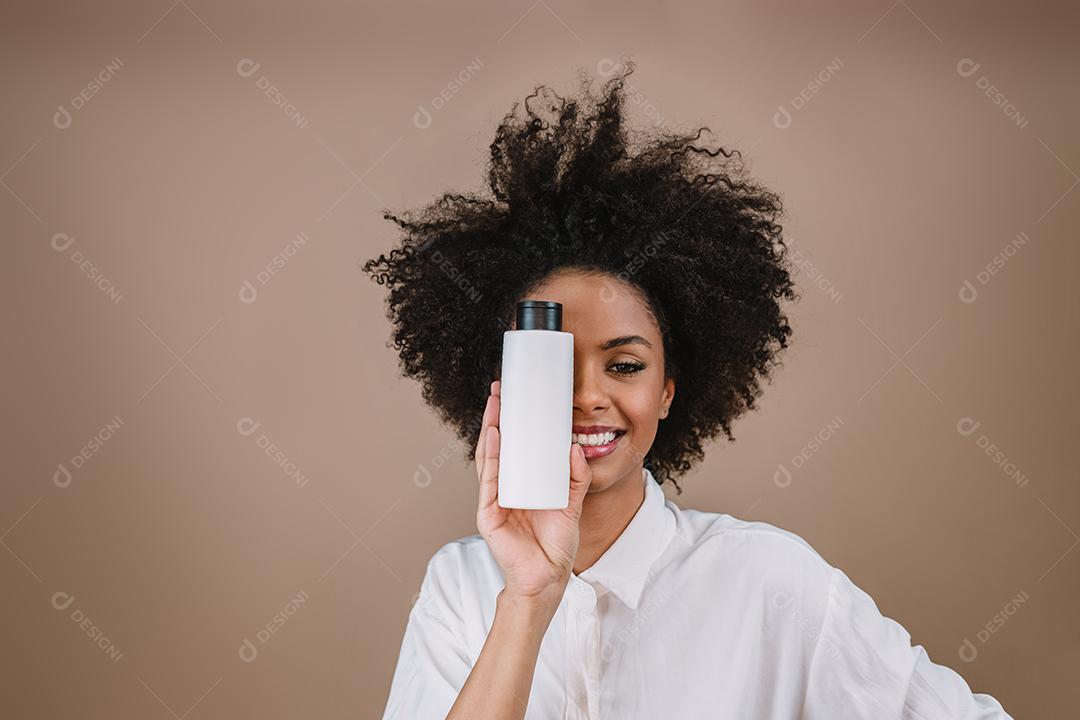 Mulher latina de beleza com penteado afro. mulher brasileira. Segurando a embalagem de xampu em branco