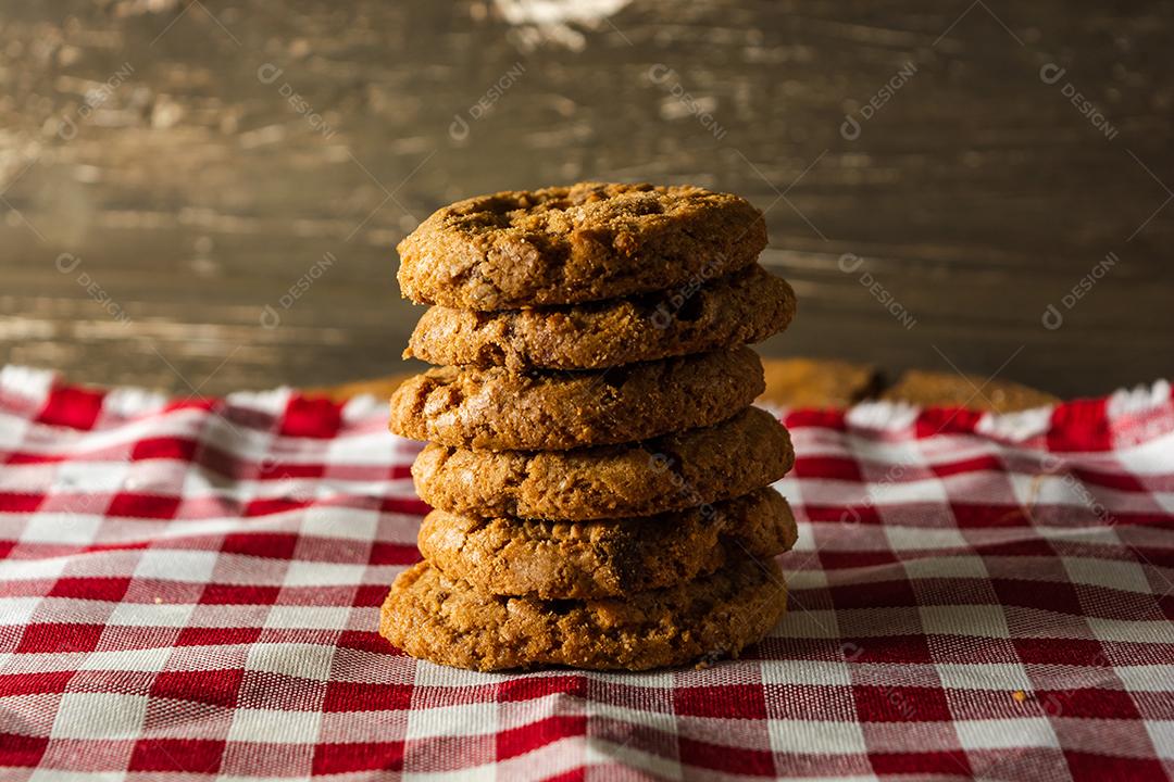 alguns biscoitos caseiros com gotas de chocolate, empilhados uns sobre os outros, na mesa de pano vermelho e fundo de madeira. conceito de café da manhã quente