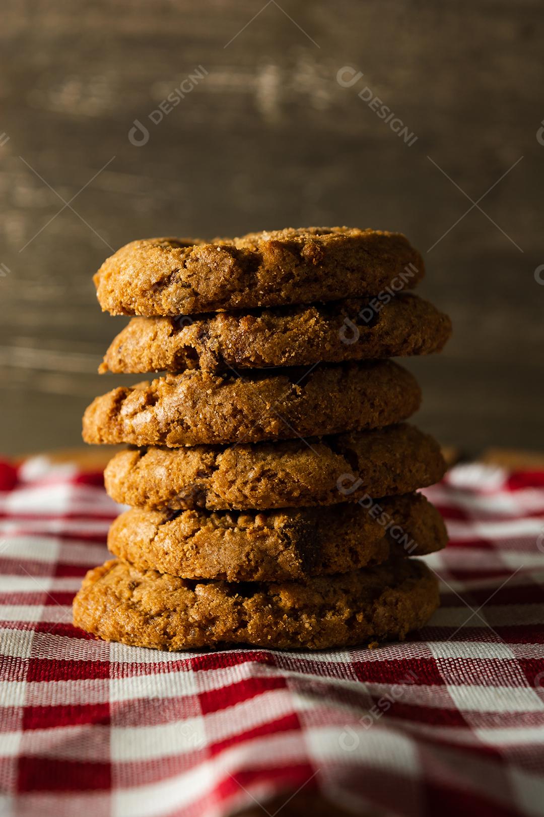 alguns biscoitos caseiros com gotas de chocolate, empilhados uns sobre os outros, na mesa de pano vermelho e fundo de madeira. conceito de café da manhã quente