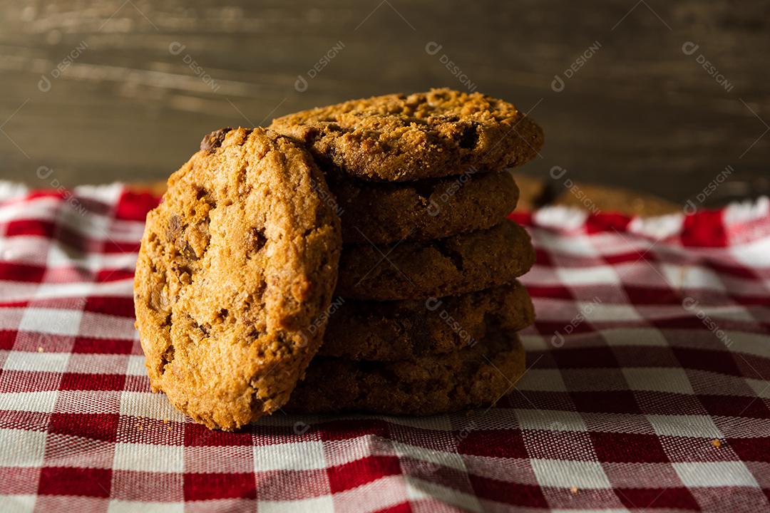 alguns biscoitos caseiros com gotas de chocolate, empilhados uns sobre os outros, na mesa de pano vermelho e fundo de madeira. conceito de café da manhã quente