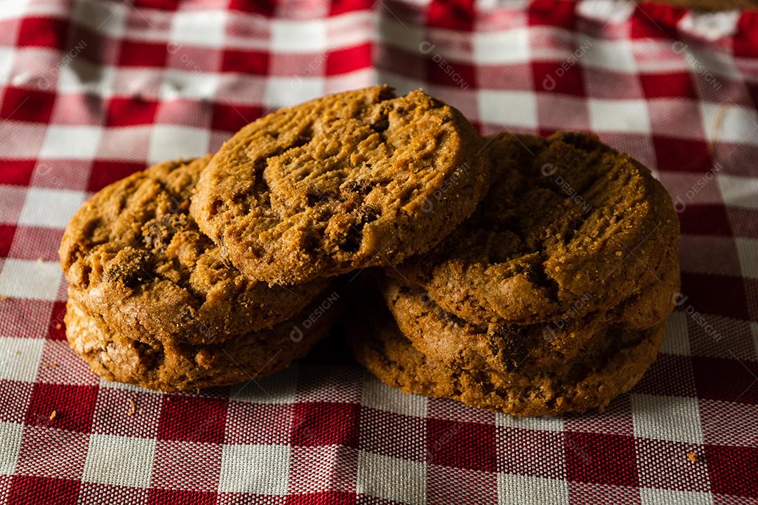alguns biscoitos caseiros com gotas de chocolate, empilhados uns sobre os outros, na mesa de pano vermelho e fundo de madeira. conceito de café da manhã quente