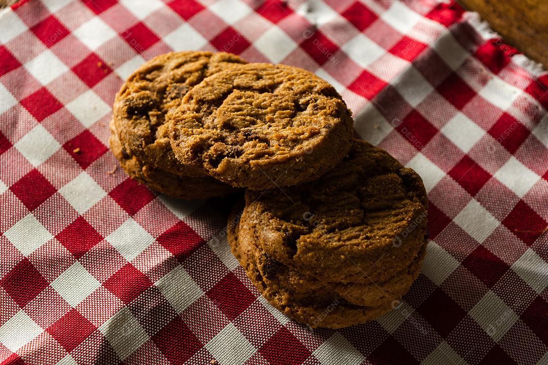 alguns biscoitos caseiros com gotas de chocolate, empilhados uns sobre os outros, na mesa de pano vermelho e fundo de madeira. conceito de café da manhã quente