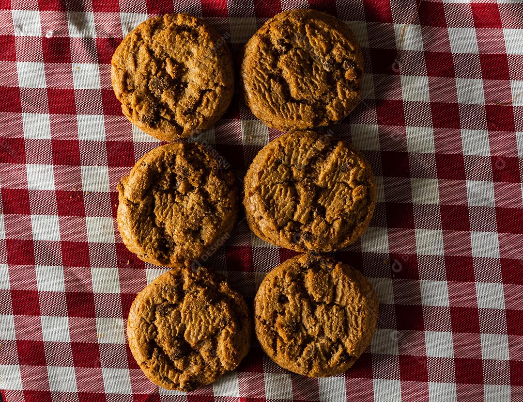 alguns biscoitos caseiros com gotas de chocolate, empilhados uns sobre os outros, na mesa de pano vermelho e fundo de madeira. conceito de café da manhã quente