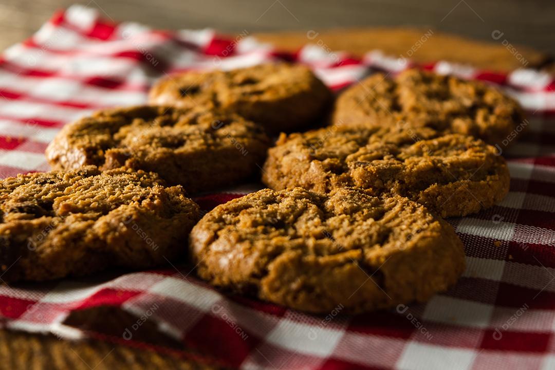 alguns biscoitos caseiros com gotas de chocolate, empilhados uns sobre os outros, na mesa de pano vermelho e fundo de madeira. conceito de café da manhã quente