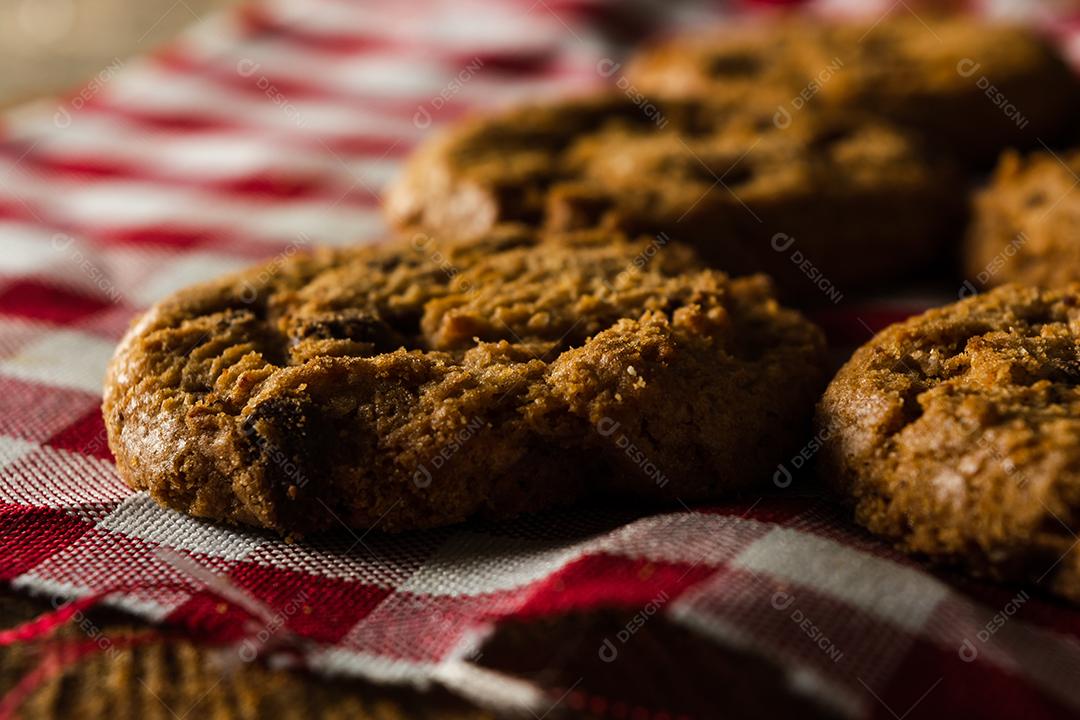 alguns biscoitos caseiros com gotas de chocolate, empilhados uns sobre os outros, na mesa de pano vermelho e fundo de madeira. conceito de café da manhã quente
