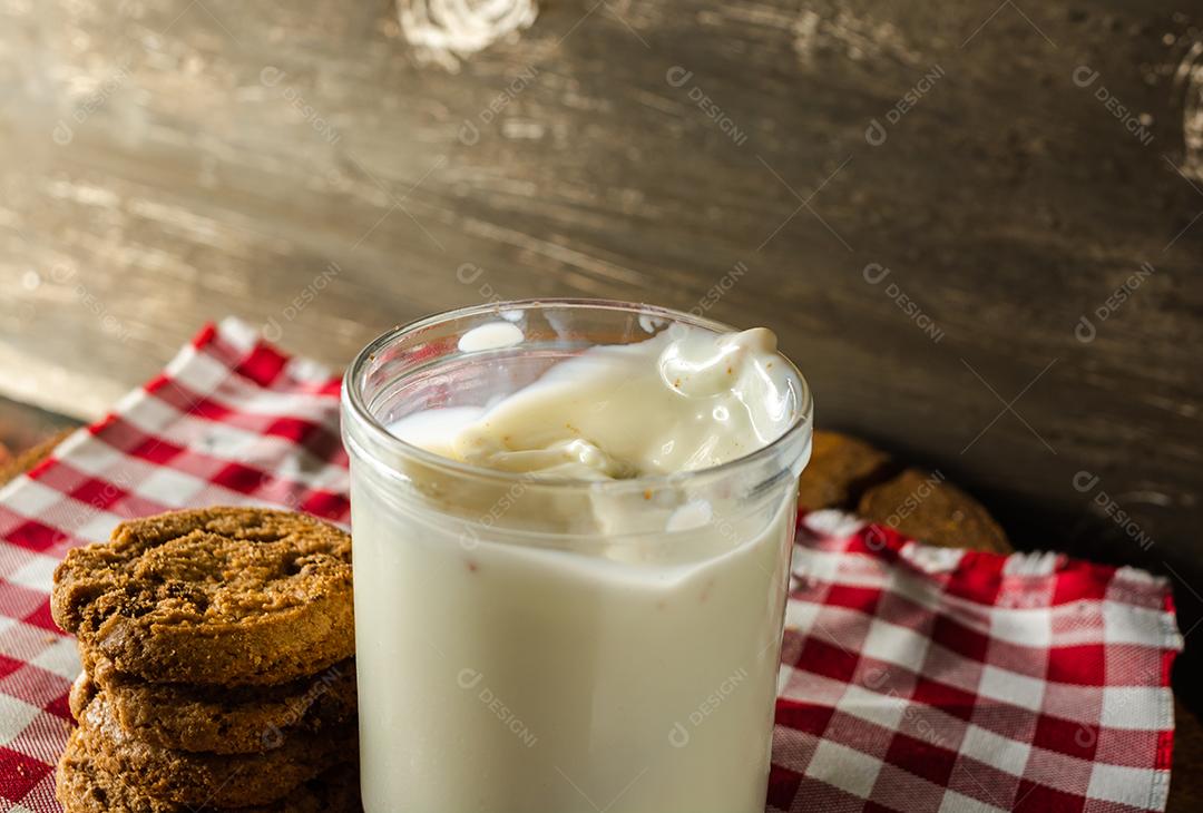alguns biscoitos caseiros com gotas de chocolate, empilhados uns sobre os outros, e um copo de leite. na mesa de pano vermelho e fundo de madeira. conceito de café da manhã quente