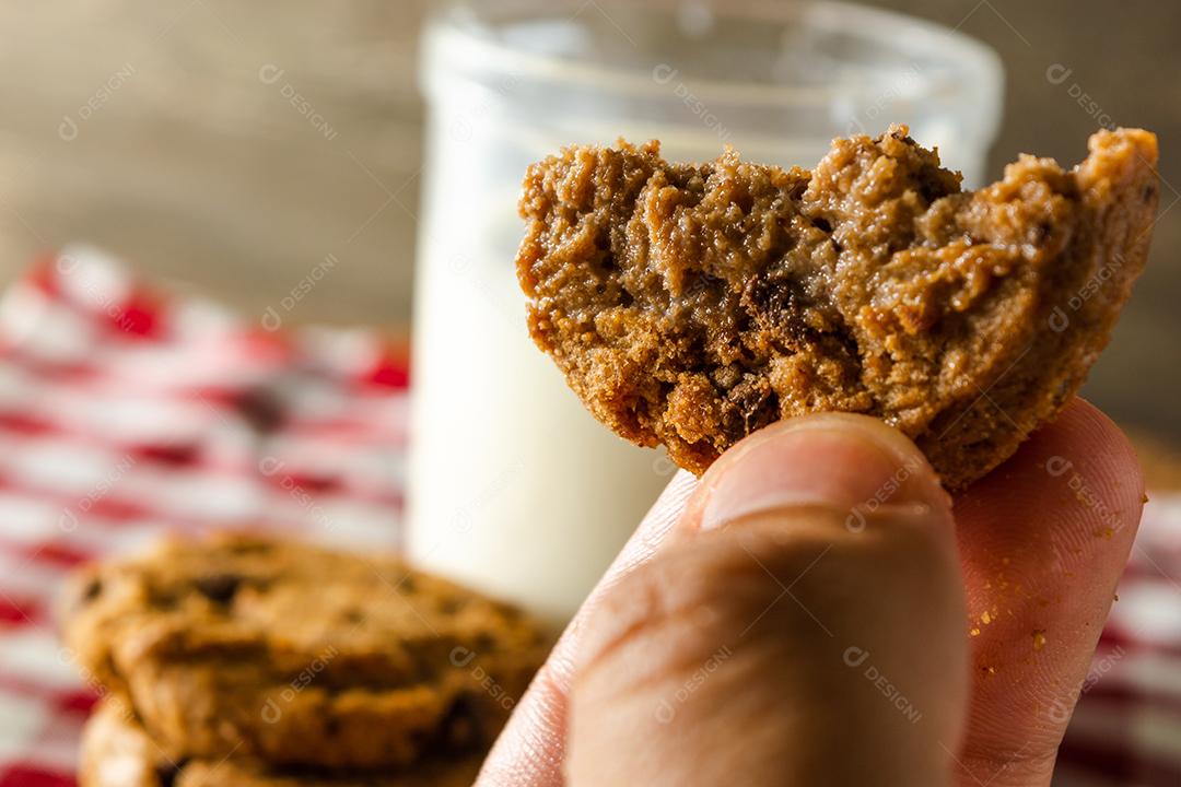 biscoitos caseiros mordidos com gotas de chocolate, empilhados uns sobre os outros, e um copo de leite. na mesa de pano vermelho e fundo de madeira. conceito de café da manhã quente